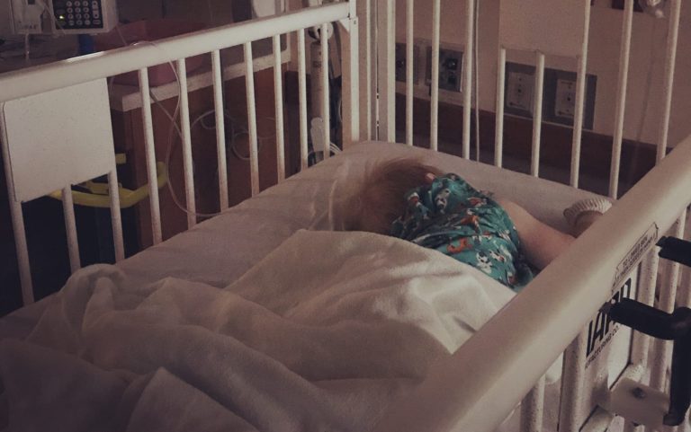 Child lying in a hospital crib surrounded by medical equipment